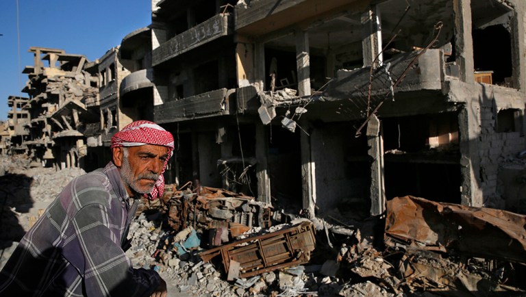 A Syrian man stands between buildings that were damaged last summer.