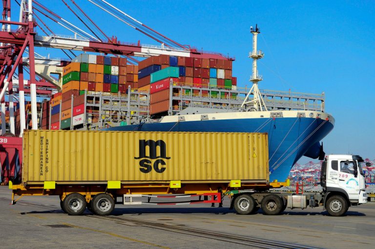 A truck transports a shipping container drives past a loaded cargo ship at a port in Qingdao in east China's Shandong province, Sunday, April 8, 2018. Amid falling markets, President Donald Trump's new economic adviser, Larry Kudlow, says there is no trade war between the U.S. and China. Another administration official, Treasury Secretary Steve Mnuchin, takes a different tack, saying he's "cautiously optimistic" that before any threatened tariffs go into place the two nations will reach an agreement. Global financial markets have fallen sharply as the world's two biggest economies square off. 