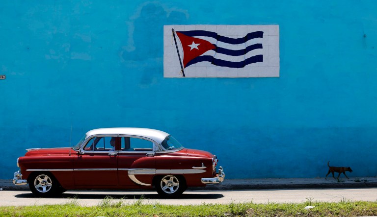 A driver steers his classic car past a wall decorated with a Cuban flag in Havana, Cuba, Sunday, June 3, 2018. 