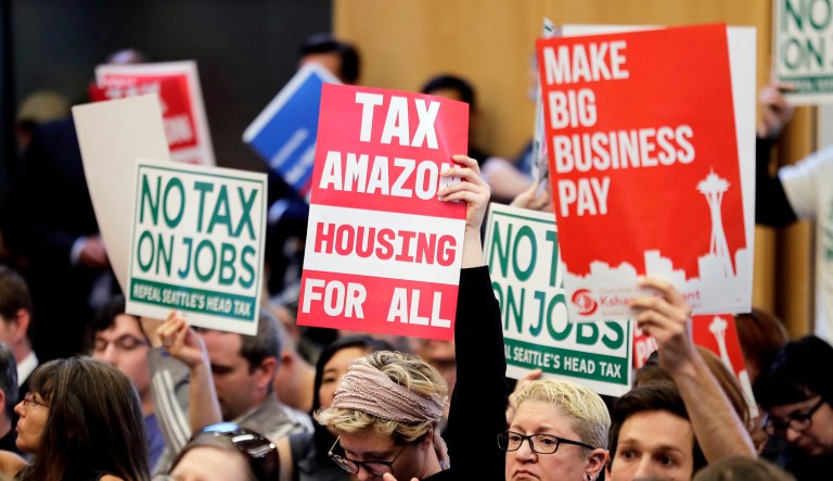 People attending a Seattle City Council meeting hold signs that read "Tax Amazon, Housing for All," and "No Tax on Jobs" listen to public comment on the debate over a possible council vote whether or not to repeal of a tax on large companies such as Amazon and Starbucks that was intended to combat a growing homelessness crisis on Tuesday at City Hall in Seattle.