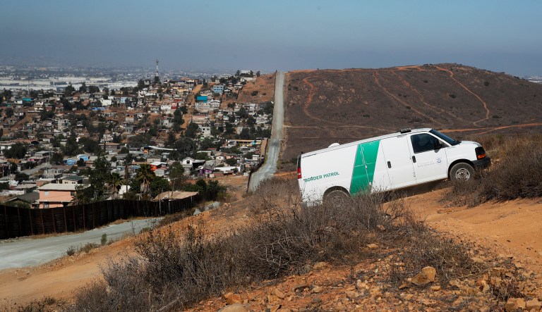 A U.S. Border Patrol van drives up the hill to pick up migrants apprehended trying to cross the U.S.-Mexico border illegally as the Mexican land looks on the left side of the border wall along a road in San Diego. 