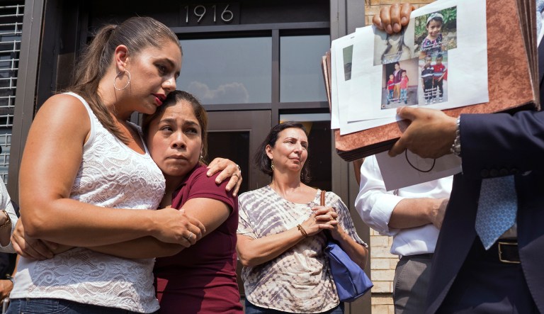 As pictures of children separated from their families are displayed, Yeni Gonzalez, a Guatemalan mother who was separated from her three children at the U.S.-Mexico border, center, is embraced by volunteer Janey Pearl, center left, during a news conference Tuesday, July 3, 2108 in New York. Gonzalez saw her children in a New York City facility for the first time since mid May.  She was driven cross-country by a team of volunteers after she was released from Eloy Detention Center in Arizona on Thursday. 