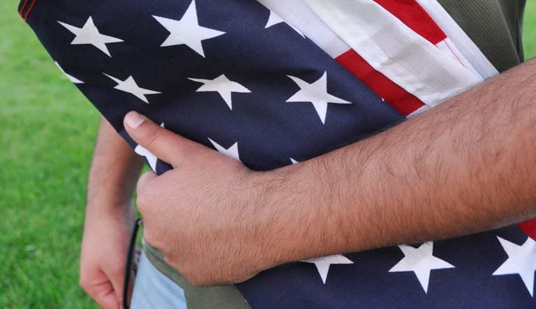 A Pakistani recruit, 22, who was recently discharged from the U.S. Army, holds an American flag as he poses for a picture. 