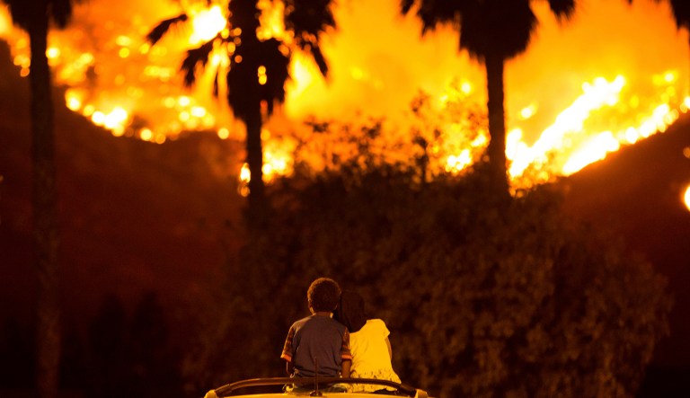 King Bass sits and watches the Holy Fire burn from on top of his parents' car as his sister Princess rests her head on his shoulder, Aug. 9, 2018, in Lake Elsinore, Calif.