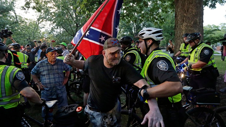A police officer grabs a man holding a Confederate flag during a rally for the recently vandalized Confederate monument known as "Silent Sam" at the University of North Carolina.
