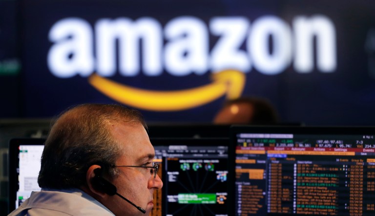 A man monitors stocks as an Amazon sign appears above his head.