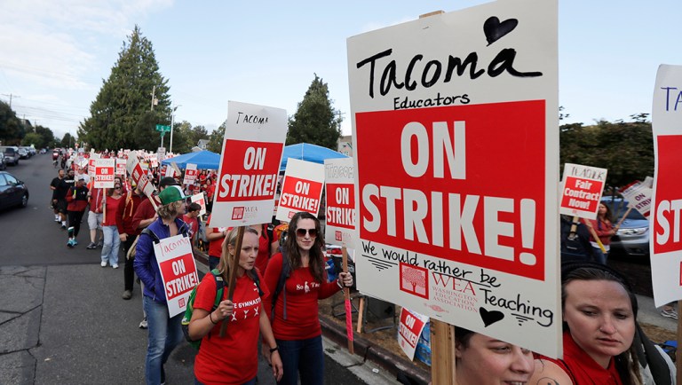 Striking teachers carry picket signs as they march around the Tacoma School District Central Administration Building.