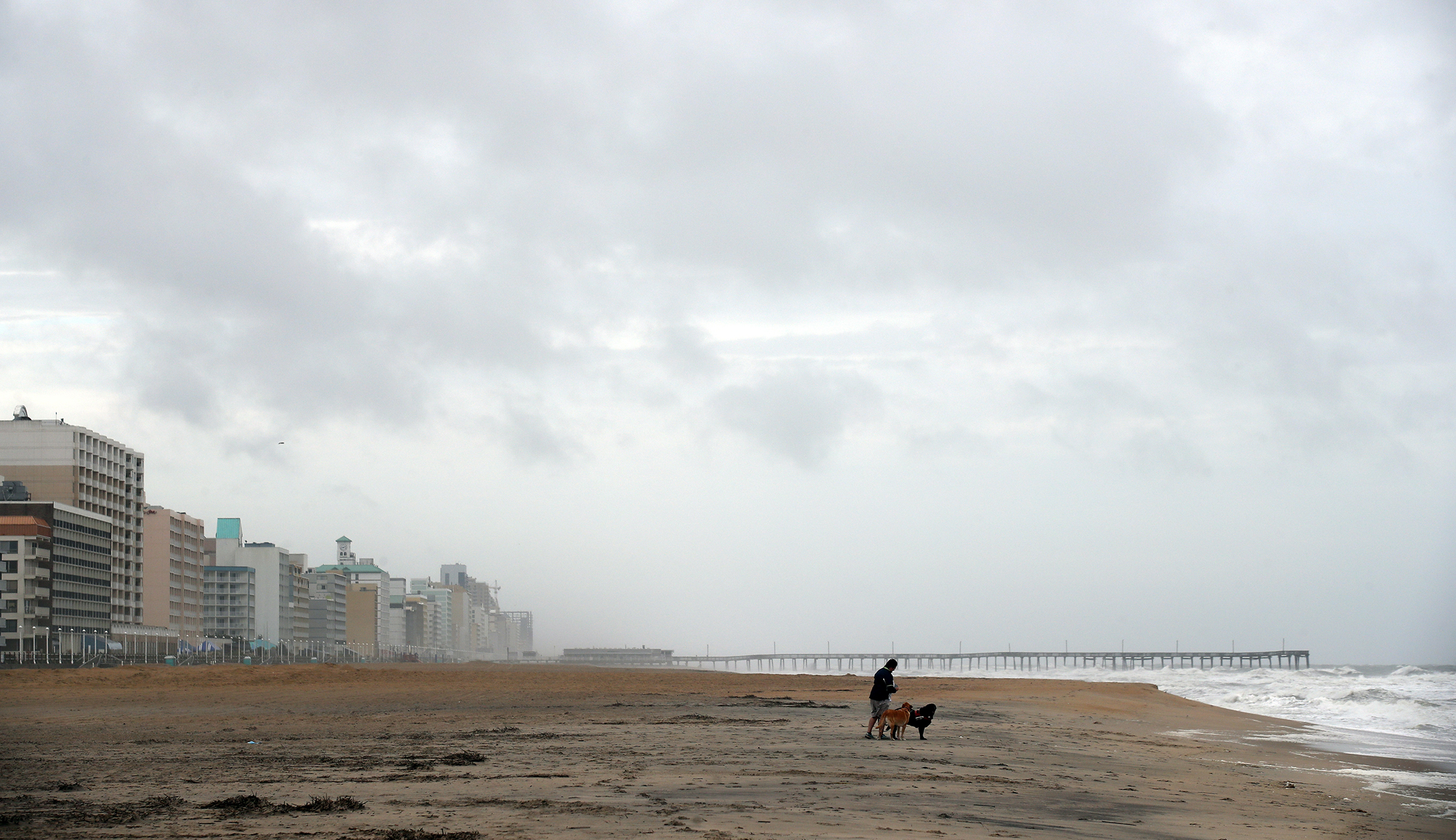 Kelly McGuire walks her dogs Jack and Roxy on a mostly deserted oceanfront beach, Friday, Sept. 14, 2018, in Virginia Beach, Va., as the effects of Hurricane Florence are felt.