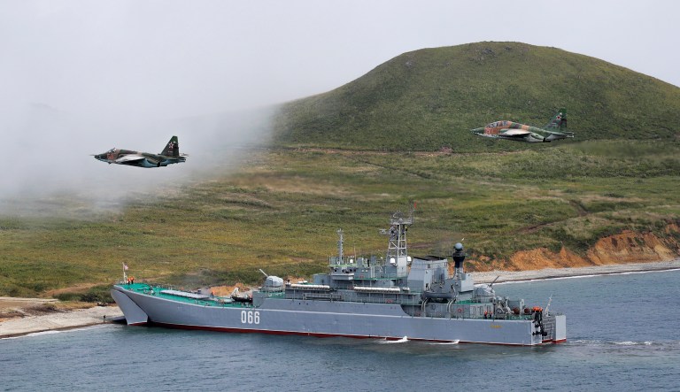 A Russian navy landing vessel unloads an armored vehicle as military helicopters fly overhead during Russian military maneuvers Vostok 2018 on the training ground "Klerk", about 50 kilometers (31 miles)south of Vladivostok, Russian Far East port, Russia, Saturday, Sept. 15, 2018 . The weeklong Vostok 2018 maneuvers are Russia's biggest-ever war games.