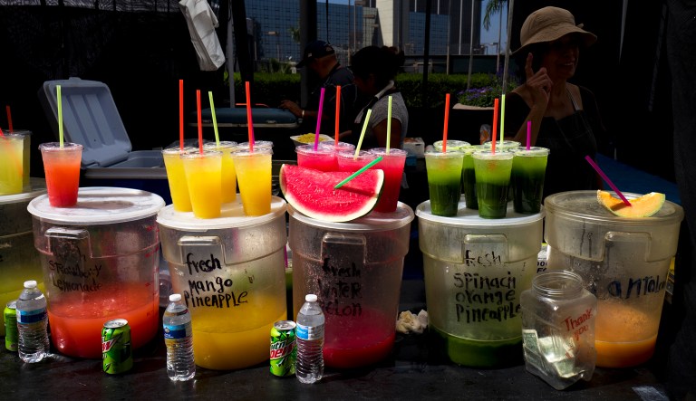 A vendor sells fresh juices and fruit with straws on top at a Farmers Market in downtown Los Angeles.
