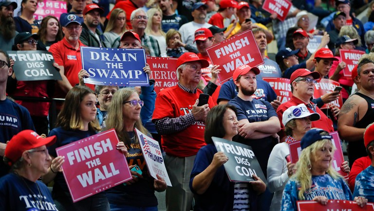Supporters stand up and holds signs as they wait to hear from President Trump.