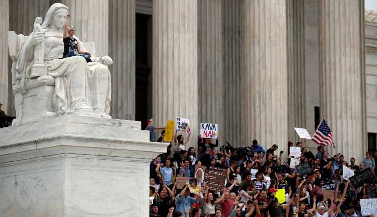 A protester sits in the lap of the Contemplation of Justice statue as activists protest on the steps of the Supreme Court after the confirmation vote of Supreme Court Justice Brett Kavanaugh, Saturday, Oct. 6, 2018 in Washington.