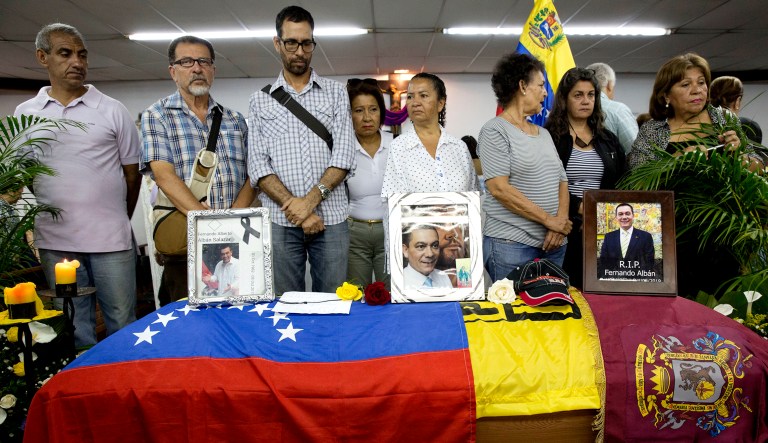 Friends, relatives, and opposition leaders stand next to the flag-draped casket containing the remains of opposition activist Fernando Alban, during his funeral at a church in Caracas, Venezuela, on Wednesday. Hundreds gathered to pay their respects to Alban. International condemnation of Venezuela's leadership poured in Tuesday following the suspicious death of the opposition activist authorities say evaded justice by throwing himself from the 10th floor of a police building. 