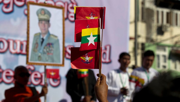 A supporter holds flags of Myanmar National and military while a portrait of Senior Gen. Min Aung Hlaing displays in the background during a pro-military rally.