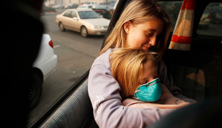 Dakota Keltner, right, rests on Havyn Cargill-Morris in a truck at a makeshift encampment outside a Walmart store for people displaced by the Camp fire, Friday, Nov. 16, 2018, in Chico, Calif. The two, from Magalia, Calif., escaped the fire with their families.