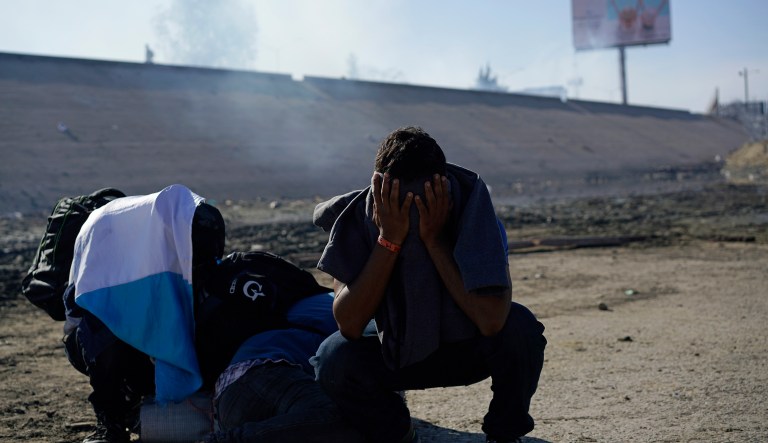 Three Honduran migrants huddle in the riverbank amid tear gas fired by U.S. agents on the Mexico-U.S. border after they and a group of migrants got past Mexican police at the Chaparral border crossing in Tijuana, Mexico, Sunday, Nov. 25, 2018. The mayor of Tijuana has declared a humanitarian crisis in his border city and says that he has asked the United Nations for aid to deal with the approximately 5,000 Central American migrants who have arrived in the city.