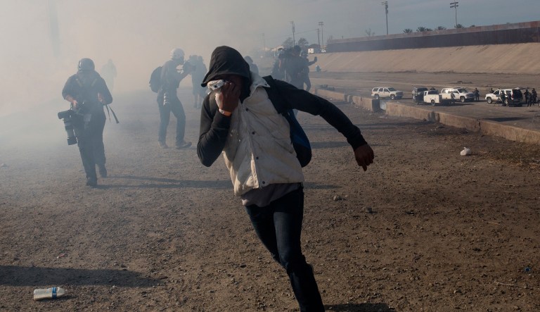 A migrant runs from tear gas launched by U.S. agents, amid members of the press covering the Mexico-U.S. border.