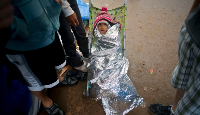 A child, who is part of the Central American migrant caravan, sits in a stroller wrapped in a reflective blanket as protection from the rain at a sports complex where more than 5,000 Central American migrants are sheltering in Tijuana, Mexico, Thursday, Nov. 29, 2018.
