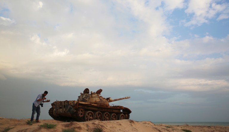 In this Wednesday, Nov. 28, 2018, photograph, a photographer changes his lens by a rusting Soviet-era tank near Mukalla, Yemen, at an airport now serving as a military base for the United Arab Emirates. The port city of Mukalla, once held by al Qaida, shows how fractious Yemen is and will remain even if the Saudi-led war in the country ends in an uneasy peace for the Arab world's poorest nation.
