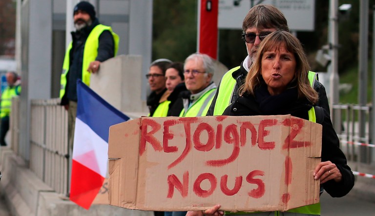 A demonstrator holds a placard reading " Join us" as they stand by toll gates on a motorway at Biarritz southwestern France, Wednesday, Dec.5, 2018. The concessions made by French president Emmanuel Macron's government in a bid to stop the huge and violent anti-government demonstrations seemed on Wednesday to have failed to convince protesters, with trade unions and disgruntled farmers now threatening to join the fray.