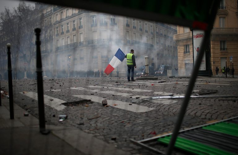 A demonstrators stands alone with a French flag during clashes Saturday, Dec. 8, 2018 in Paris. Crowds of yellow-vested protesters angry at President Emmanuel Macron and France's high taxes tried to converge on the presidential palace Saturday, some scuffling with police firing tear gas, amid exceptional security measures aimed at preventing a repeat of last week's rioting. 