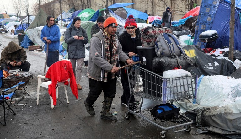 It was moving day for some at the Hiawatha homeless encampment and a day of joy and emotion for some Tuesday, Dec. 11, 2018, in Minneapolis, Minn. James Loerzel, 59, center rear, who has lived at the camp for about three months, is interviewed by a journalist while members of Natives Against Heroin move his belongings for the move to the new navigation center site.