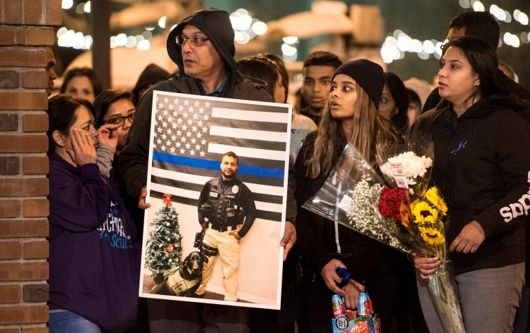 In this Friday, Dec. 28, 2018, photo, family members of police Cpl. Ronil Singh including Birend Singh, holding picture at left, attend a candlelight vigil for the slain officer in downtown Newman, Calif. The killing of the California police officer has rekindled the debate about the state's sanctuary law, which limits cooperation with U.S. immigration officials.