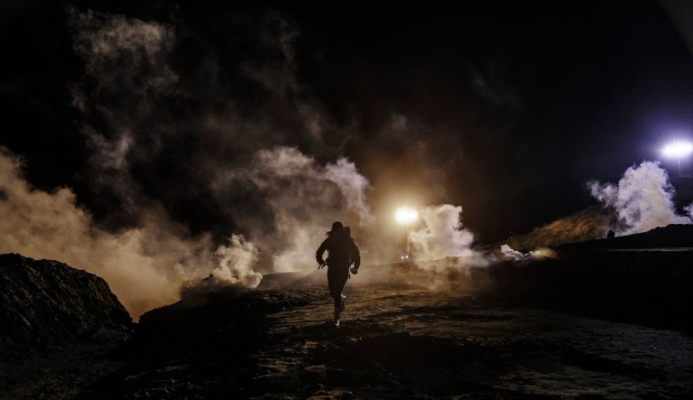 Migrants run as tear gas is thrown by U.S. Border Protection officers to the Mexican side of the border fence after they climbed the fence to get to San Diego, Calif., from Tijuana, Mexico, Tuesday, Jan. 1, 2019.