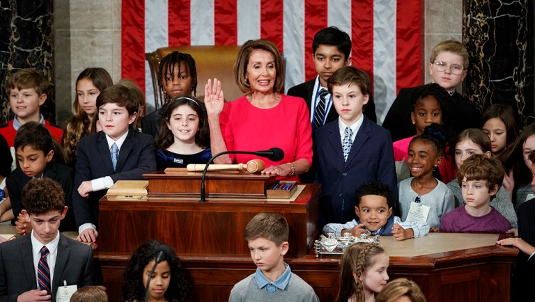 Nancy Pelosi of California, surrounded by her grandchildren and other children raises her right hand.