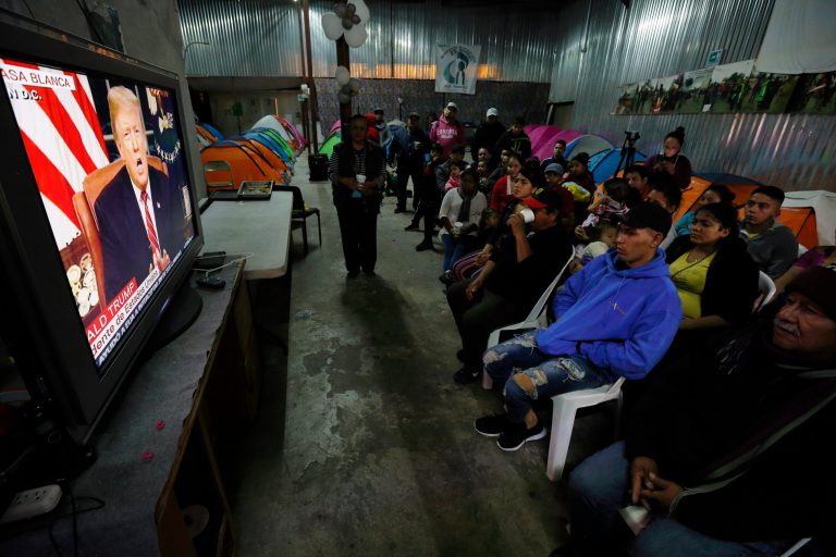 Migrants mainly from Mexico and Central America look on as U.S. President Donald Trump gives a prime-time address about border security Tuesday, Jan. 8, 2019, watching from a border migrant shelter in Tijuana, Mexico.