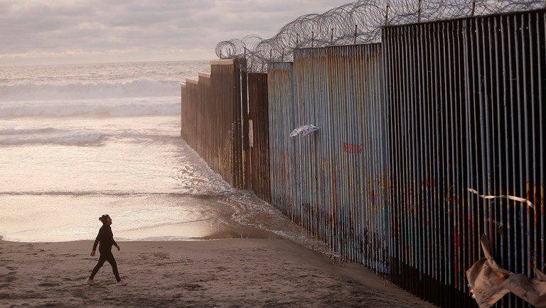 A woman walks on the beach next to the border wall topped with razor wire in Tijuana, Mexico.