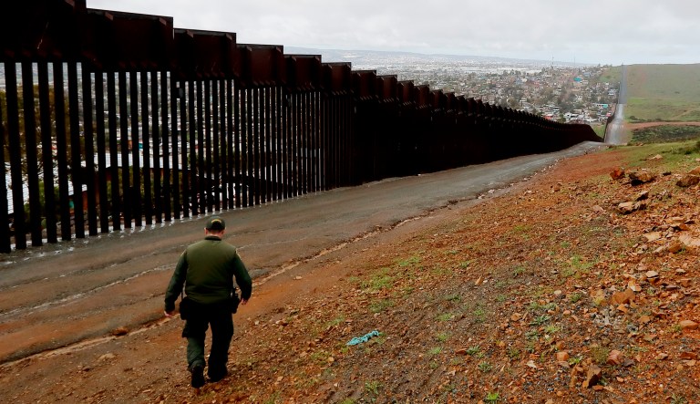 An officer on the American side of the U.S.-Mexico border walks near a wall.