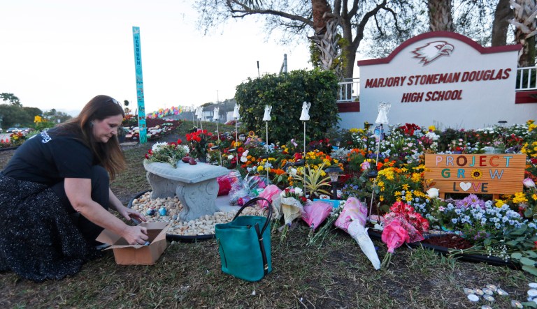Suzanne Devine Clark, an art teacher at Deerfield Beach Elementary School, places painted stones at a memorial outside Marjory Stoneman Douglas High School during the one-year anniversary of the school shooting, Thursday, Feb. 14, 2019, in Parkland, Fla.