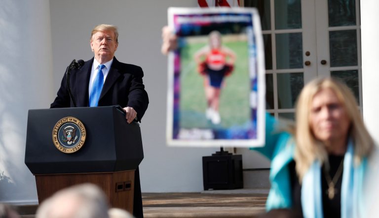 President Donald Trump looks on as an Angel Mom holds up a poster of her daughter, during an event in the Rose Garden at the White House to declare a national emergency in order to build a wall along the southern border, Friday, Feb. 15, 2019 in Washington. 