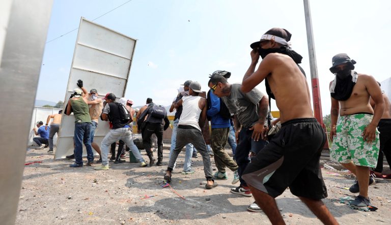 Venezuelans use a piece of metal siding as a shield after National Guard fired tear gas on residents clearing the barricaded Simon Bolivar border bridge to Colombia when they tried to deliver humanitarian aid to Venezuela despite objections from President Nicolas Maduro, in Cucuta, Colombia, Saturday, Feb. 23, 2019. 