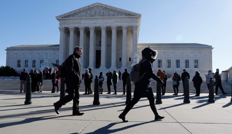 Pedestrians pass a line of people waiting to enter the Supreme Court, Monday, Feb. 25, 2019, in Washington. 