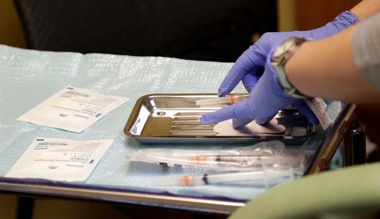 A healthcare worker prepares syringes, including a vaccine for measles, mumps, and rubella (MMR), for a child's inoculation.