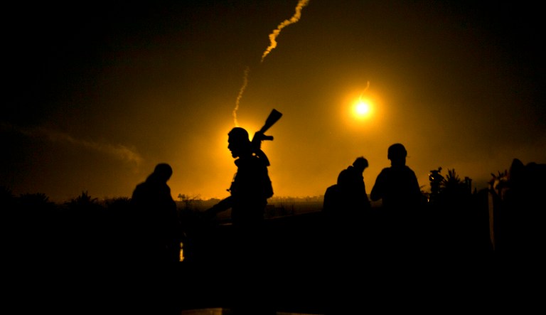 In this Tuesday, March 12, 2019 file photo, a U.S.-backed Syrian Democratic Forces (SDF) fighter watches illumination rounds light up Baghouz, Syria, as the last pocket of Islamic State militants is attacked.