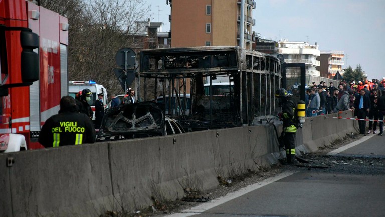 Firefighters stand by the gutted remains of a bus in San Donato Milanese.