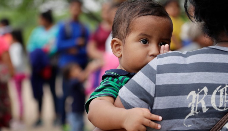 In this Thursday, March 14, 2019, photo, Lian Mejia Ruiz, 7 months, peers over the shoulder of his mother, Carmen Mejia, as they wait for Border Patrol agents to apprehend them at the U.S.-Mexico border near McAllen, Texas. Carmen Mejia said she left Honduras with her youngest son due to poverty.