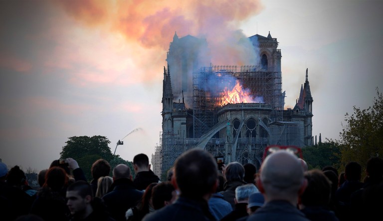People watch as flames and smoke rise from Notre Dame cathedral as it burns in Paris, Monday.