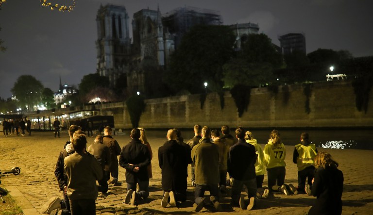 People pray on their knees by the Seine riverside in front of the Notre Dame cathedral in Paris, Tuesday, April 16, 2019. The inferno that raged through Notre Dame Cathedral for more than 12 hours destroyed its spire and its roof but spared its twin medieval bell towers, and a frantic rescue effort saved the monument's "most precious treasures," including the relic revered as Jesus' Crown of Thorns, officials said Tuesday.