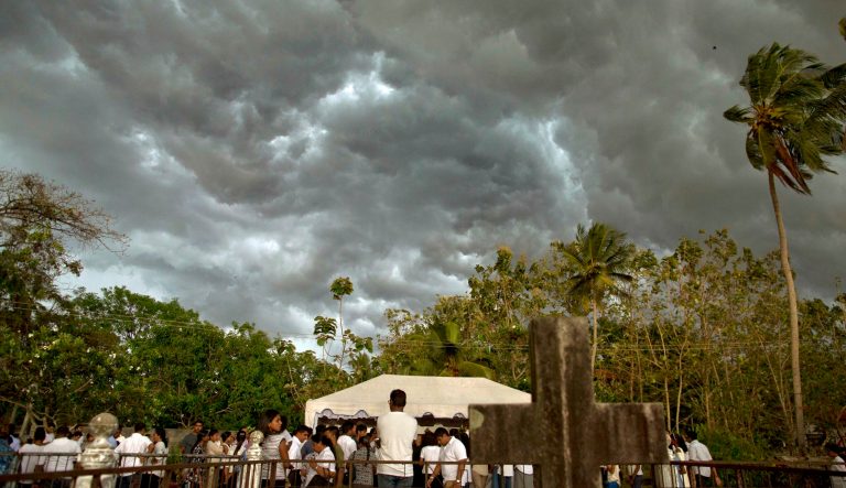 Dark clouds accumulate as people gather to bury three members of the same family, all died at Easter Sunday bomb blast at St. Sebastian Church in Negombo, Sri Lanka, Monday, April 22, 2019. Easter Sunday bombings of churches, luxury hotels and other sites was Sri Lanka's deadliest violence since a devastating civil war in the South Asian island nation ended a decade ago. 