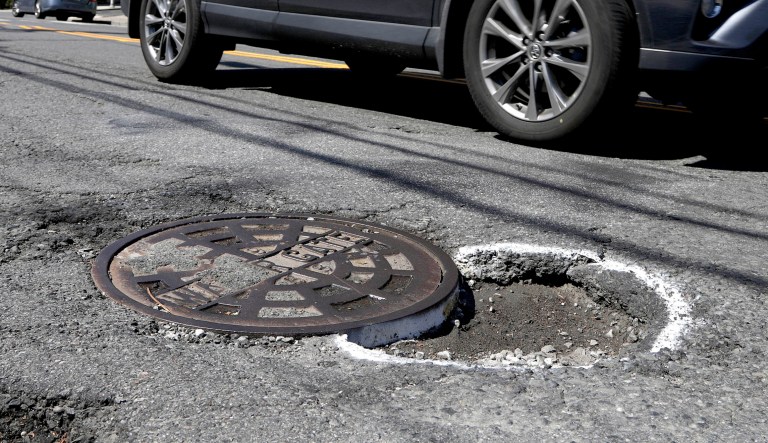 A vehicle maneuvers around a pothole outlined by paint near a manhole.
