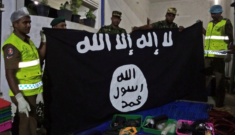 In this Friday, April 26, 2019, photo, Sri Lankan police officers show ISIS flag recovered from alleged hideout of militants, in Kalmunai, in Eastern Sri Lanka. Militants linked to Easter suicide bombings opened fire and set off explosives during a raid by Sri Lankan security forces on a house in the country's east.