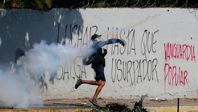 An anti-government protester returns a tear gas canister launched by security forces to disperse demonstrators in Caracas, Venezuela.