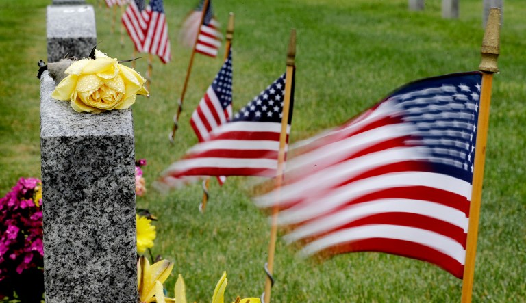 Rain drops stand out on a yellow rose as flags flutter in the wind next to the gravestone of Oliver Hickles, who served in World War II and Korea in the U.S. Army, at Tahoma National Cemetery in Kent, Wash.