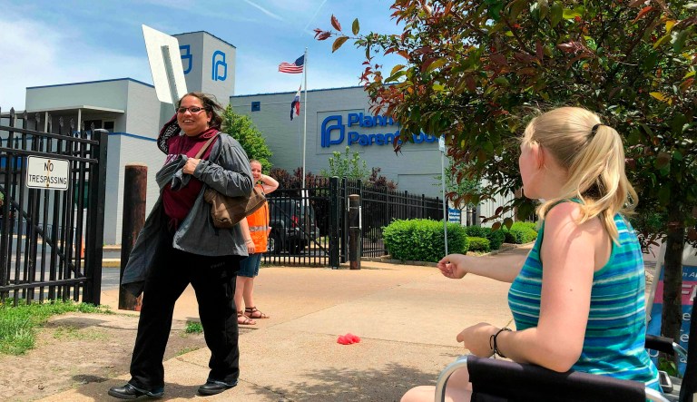 FILE - In this May 17, 2019 file photo, Teresa Pettis, right, greets a passerby outside the Planned Parenthood clinic in St. Louis. Pettis was one of a small number of abortion opponents protesting outside the clinic on the day the Missouri Legislature passed a sweeping measure banning abortions at eight weeks of pregnancy. Planned Parenthood says Missouri's only abortion clinic could be closed by the end of the week because the state is threatening to not renew its license, which expires Friday, May 31.