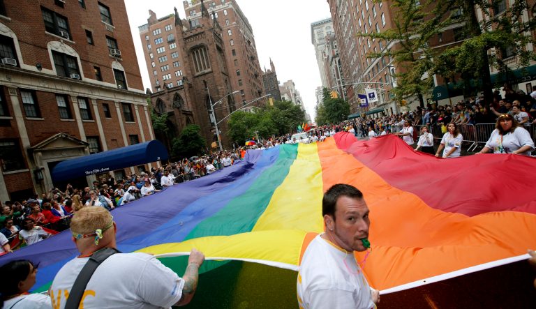 In this June 28, 2015 photo, participants carry a rainbow-colored flag down Fifth Avenue in New York during the Heritage Pride March in New York. 