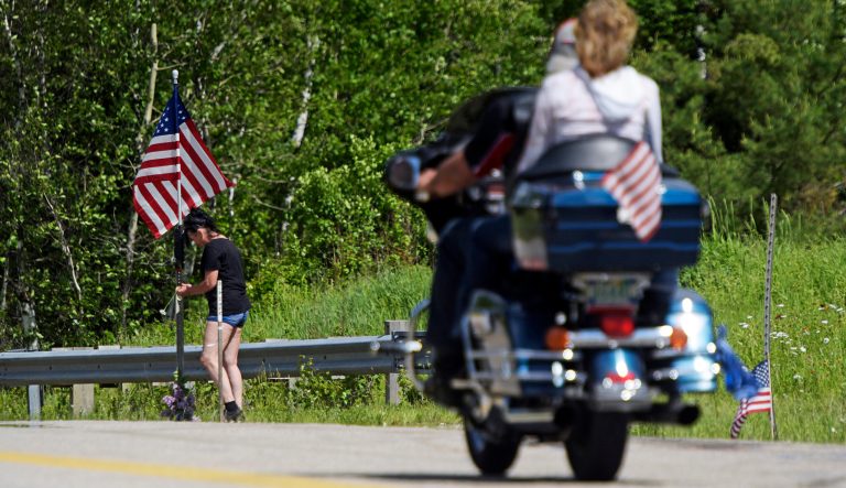 A motorcycle passes as a woman leaves flowers at the scene of a fatal accident on Route 2 in Randolph, N.H., Saturday, June 22, 2019. 